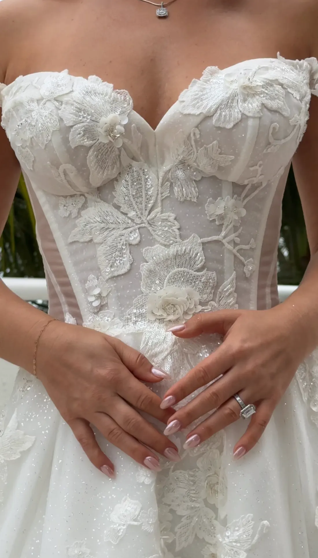 Close detail of a lace bodice with the bride's hands and engagement ring