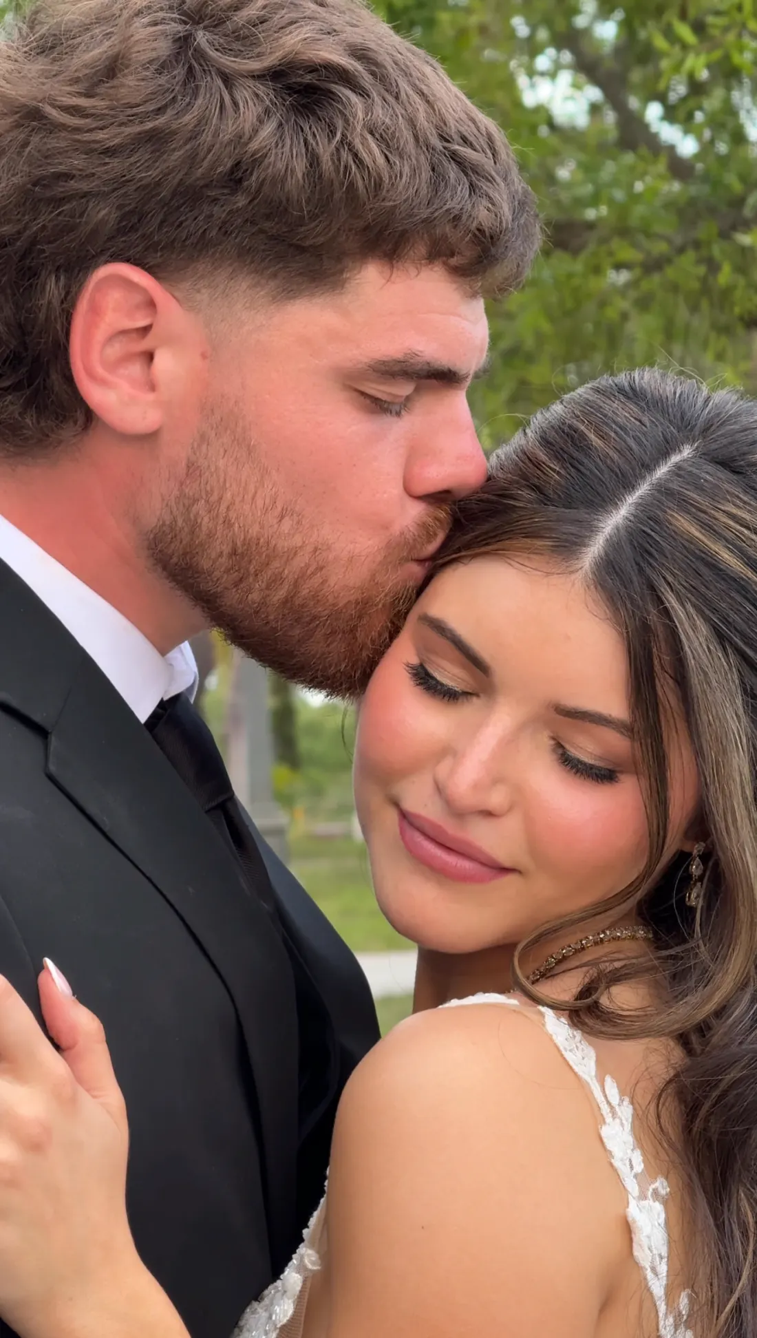 Groom kissing bride's temple as she smiles with eyes closed