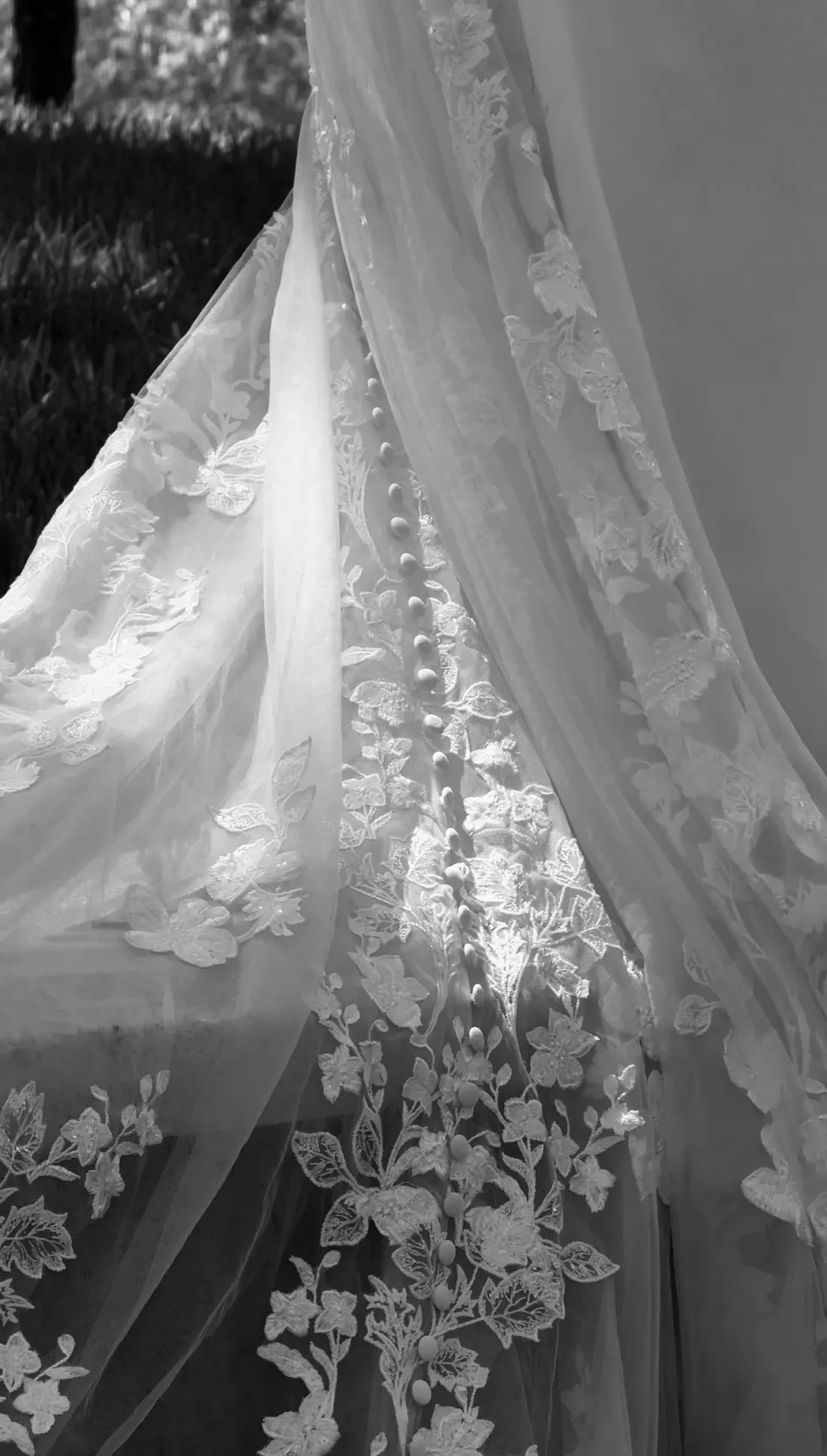 Black and white detail of a lace wedding train with covered buttons