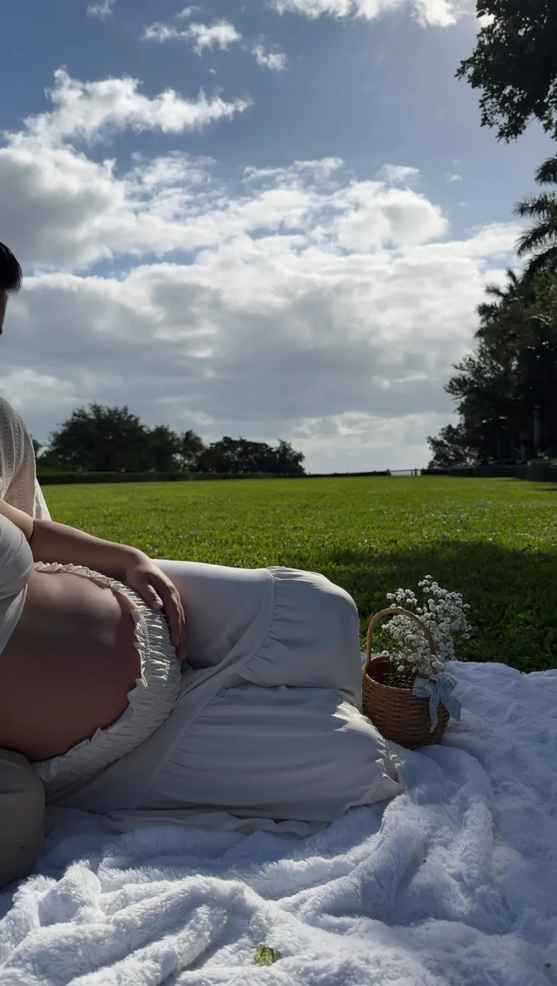 Maternity picnic on a white blanket beneath a bright cloudy sky