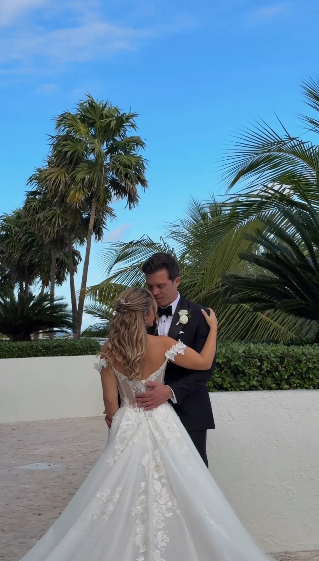 Couple embracing among palms, the bride's lace gown in the foreground
