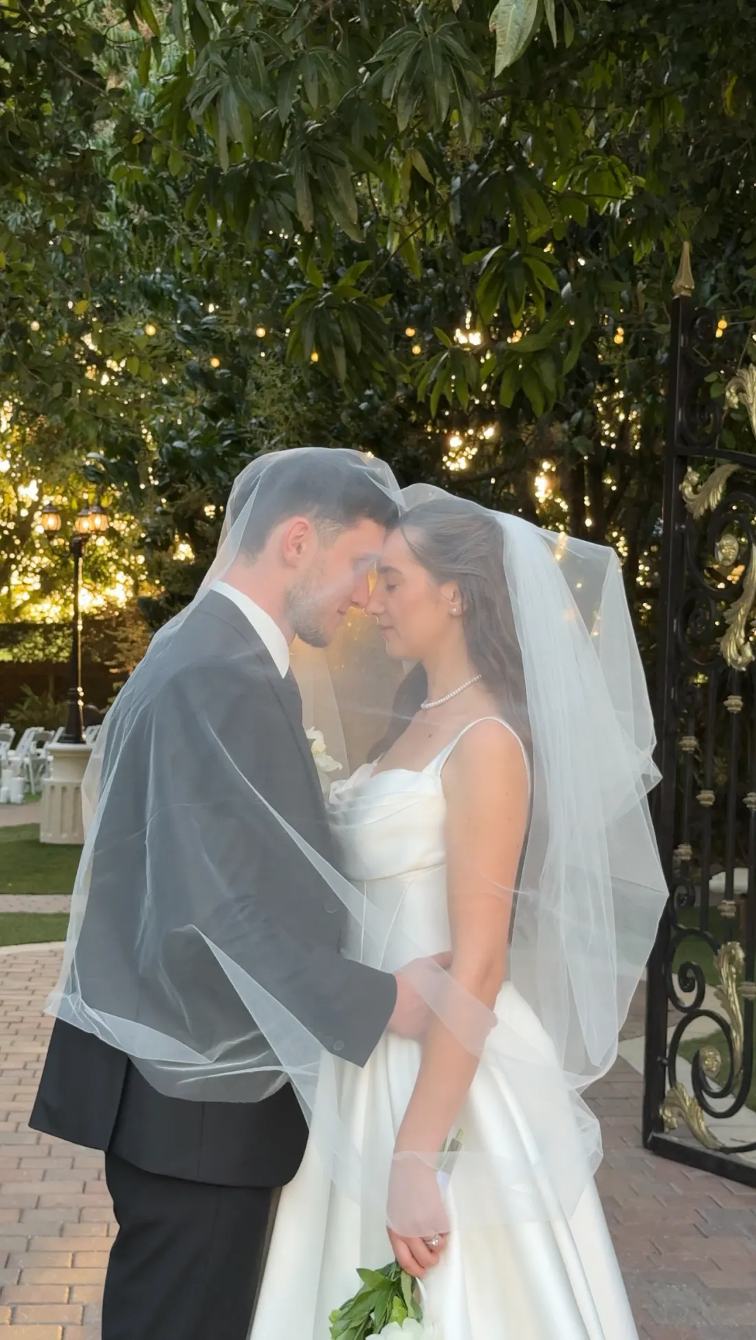 Couple sheltered under the veil beside an ornate garden gate